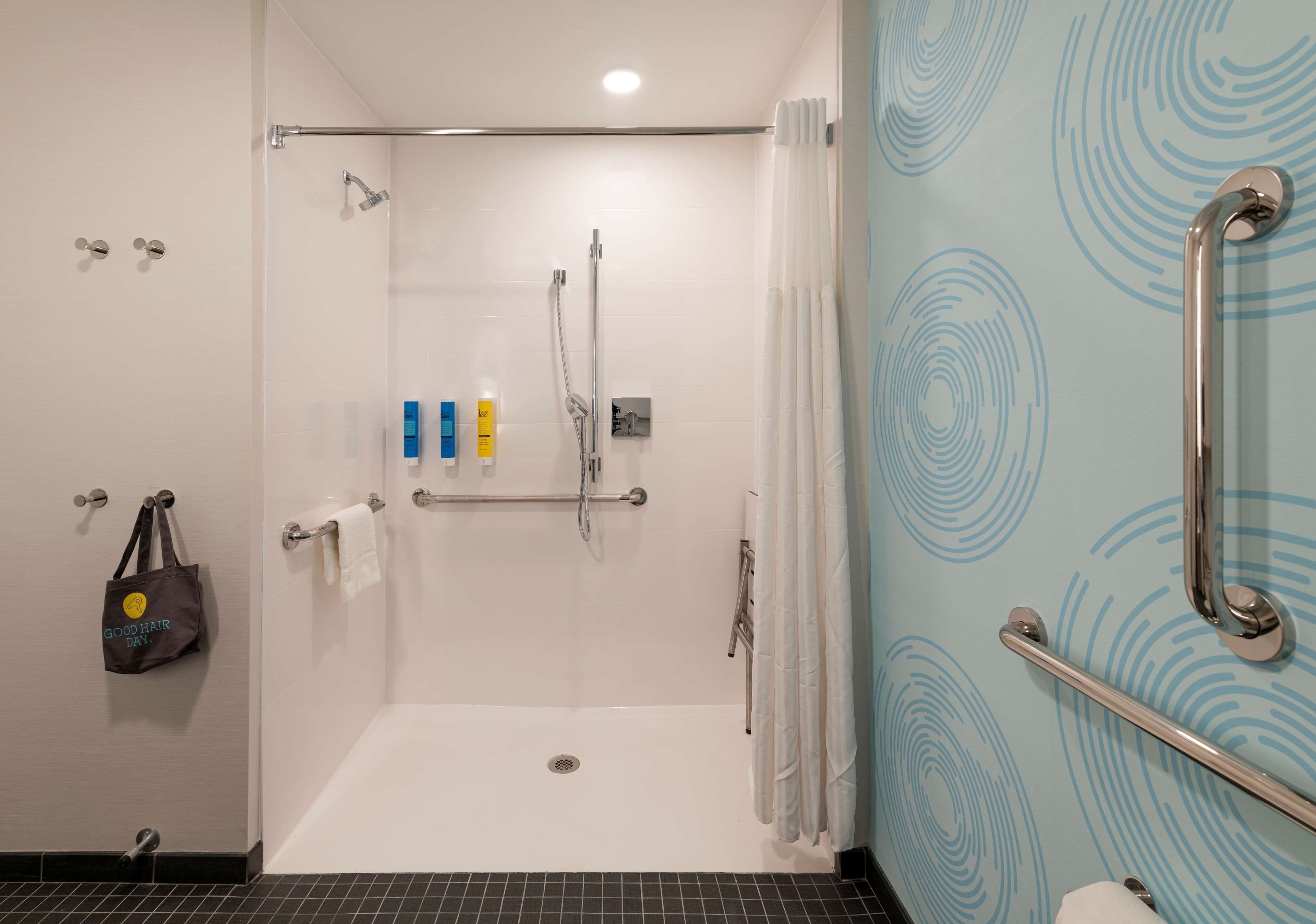 A modern bathroom with a shower, grab bars, a towel rack, and a hand sanitizer dispenser.