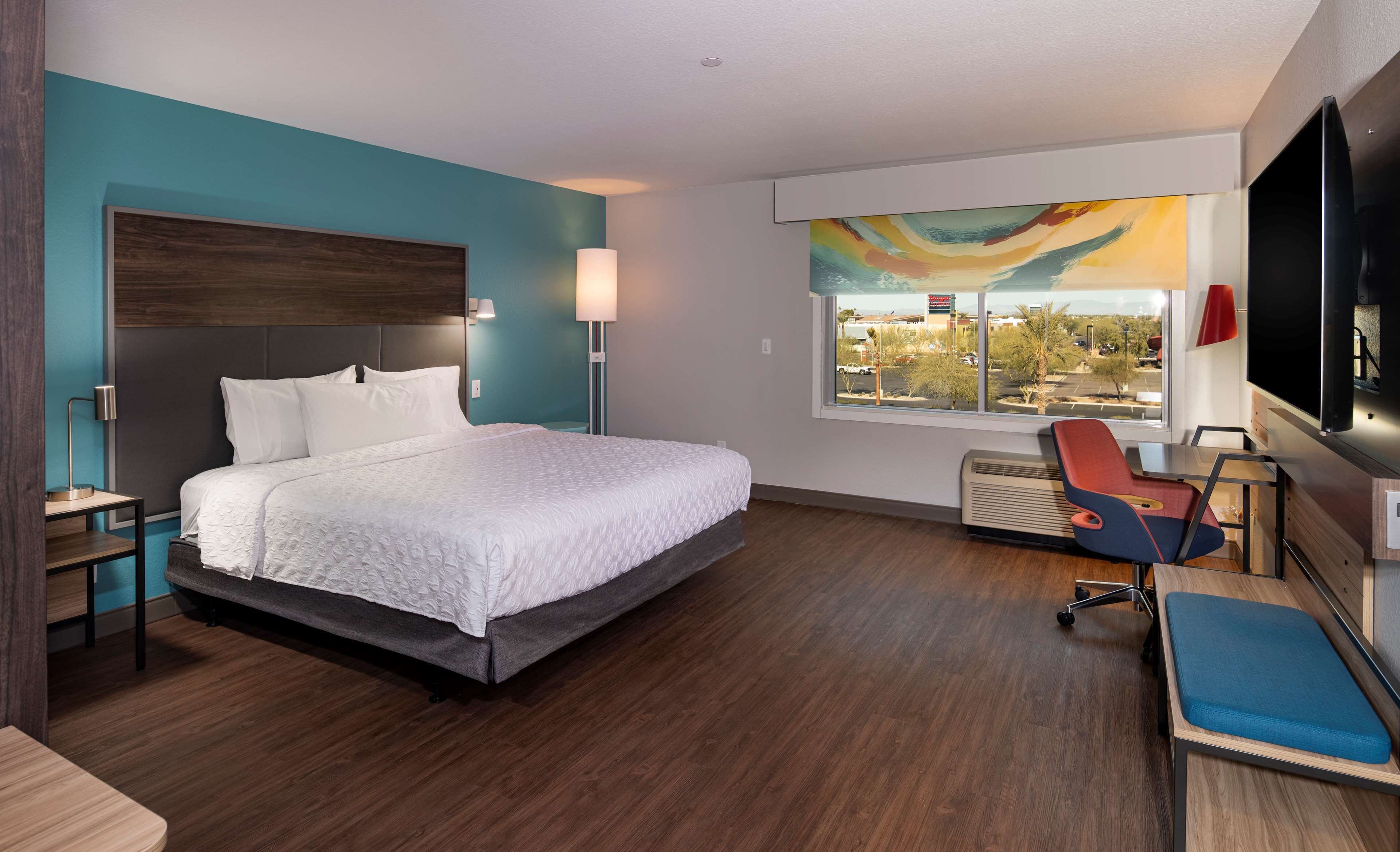 A modern hotel room with a large bed, a desk, a chair, and a window with a city view.