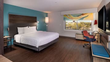 A modern hotel room with a large bed, a desk, a chair, and a window with a city view.
