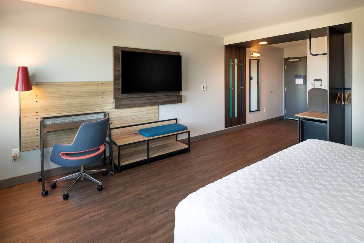 Ein Hotelzimmer mit einem Bett, einem Schreibtisch mit Stuhl, einem an der Wand befestigten Fernseher und einer Tür zu einem Badezimmer.