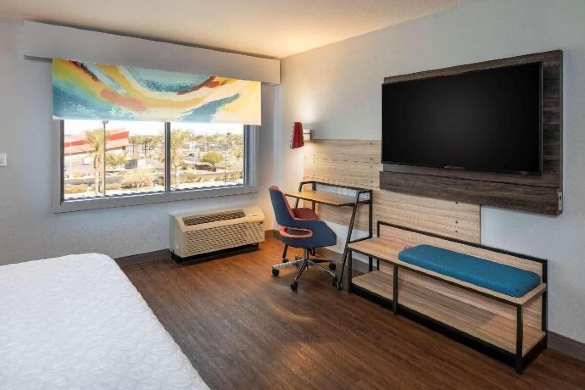A hotel room with a bed, a desk, a chair, a TV, and a window with a view.