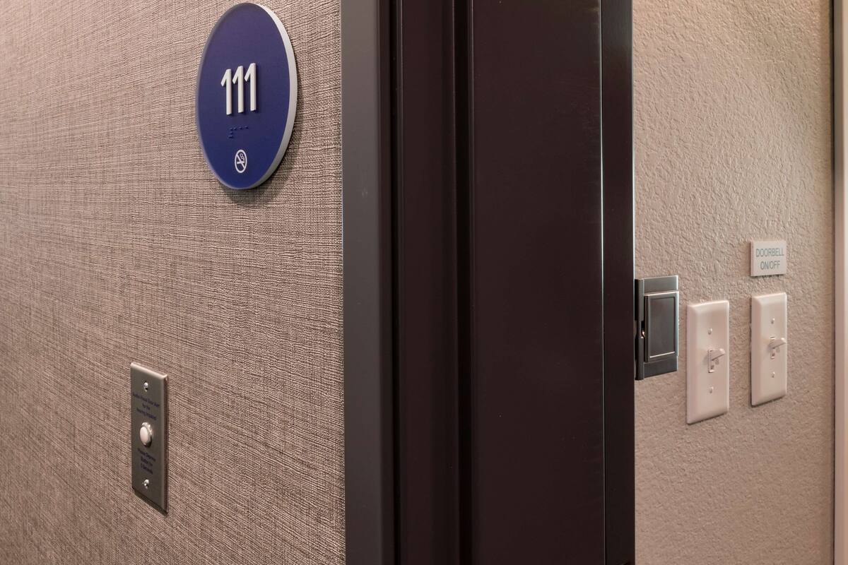 Innenansicht eines Hotelaufzugs mit einem blauen Schild, das die Zimmernummer 111 anzeigt, einem Klingelknopf und einem Klingelschalter an der Wand.