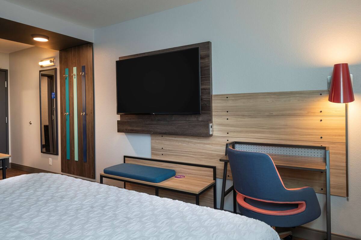 Ein Hotelzimmer mit Bett, Schreibtisch, Stuhl, einem an der Wand befestigten Fernseher und einer roten Lampe.