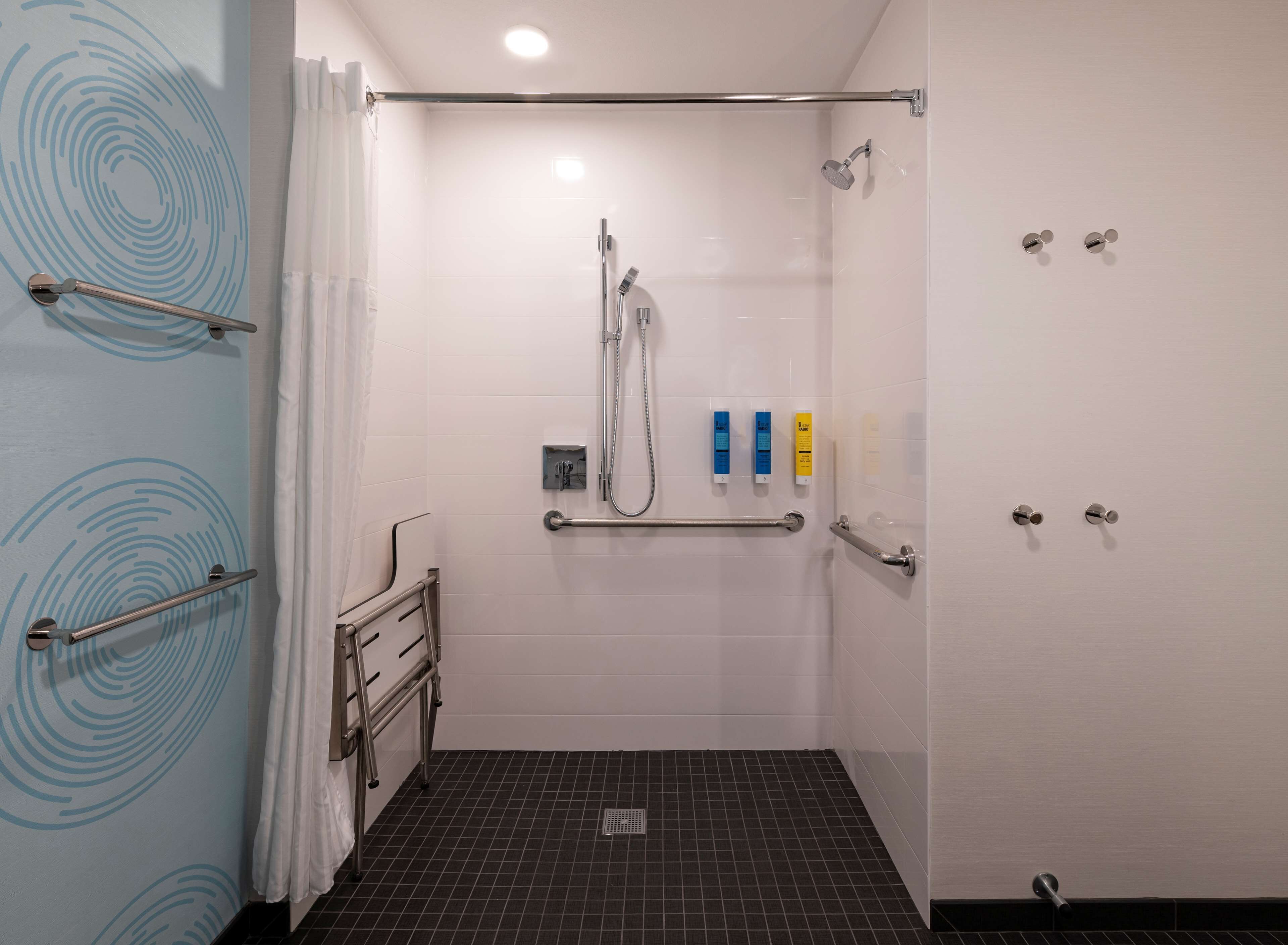 A modern bathroom with a shower, grab bars, and a hand dryer.