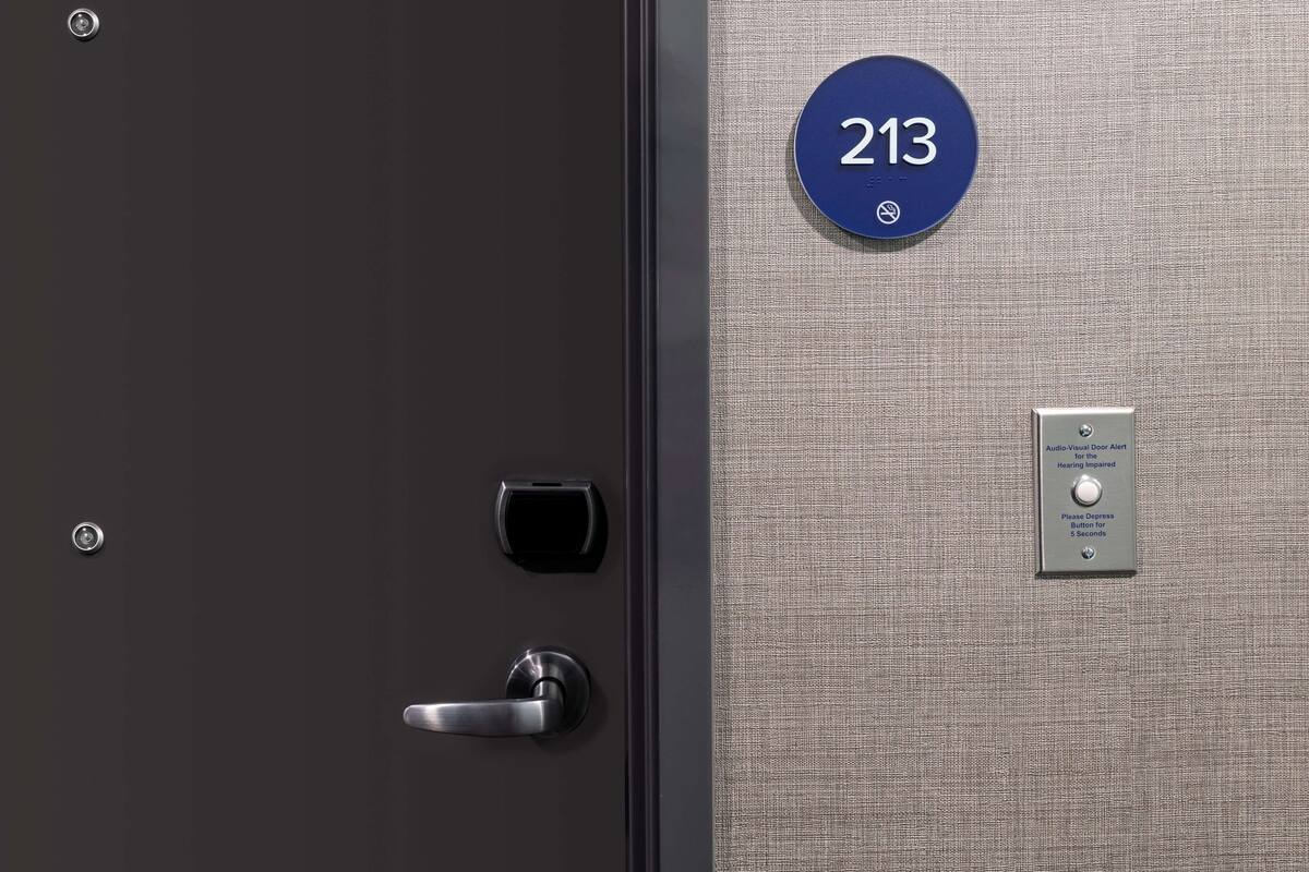 Eine Hotelzimmertür mit digitalem Schloss, Schlüsselloch und einer Nummernschild mit der Zimmernummer 213.