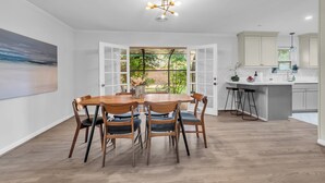 Une cuisine moderne avec des meubles blancs, un îlot central et un coin repas comprenant une table et des chaises en bois.
