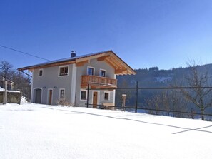 A two-story house with a balcony, surrounded by snow and a mountainous backdrop.