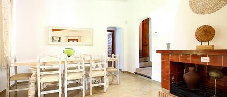 A dining area with a wooden table and chairs, a fireplace with a vase, and a mirror on the wall.