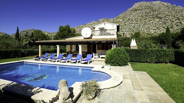 A pool area with lounge chairs, a building with a mountain backdrop, and a clear sky. - BARRACA. Haven of peace 10 just min. walk to the centre (Puerto Pollensa)