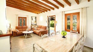 A spacious living room with a wooden ceiling, a sofa set, a coffee table, and a dining table with chairs. - BARRACA. Haven of peace 10 just min. walk to the centre (Puerto Pollensa)