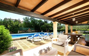 Een buitenzwembad met ligbedden, een tafel en een pergola.