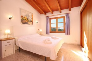 A bedroom with a bed, nightstands, wall-mounted lamps, a window with curtains, and a painting on the wall.