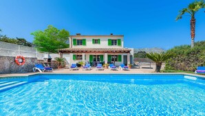 A swimming pool with lounge chairs, a house with green shutters, and a lifebuoy on the wall. - LLORENS (IVANA).  5 bedroom villa to enjoy with family and friends (Pollensa)