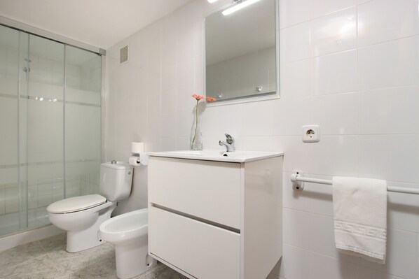 Un baño con inodoro, bidé y cabina de ducha de vidrio.