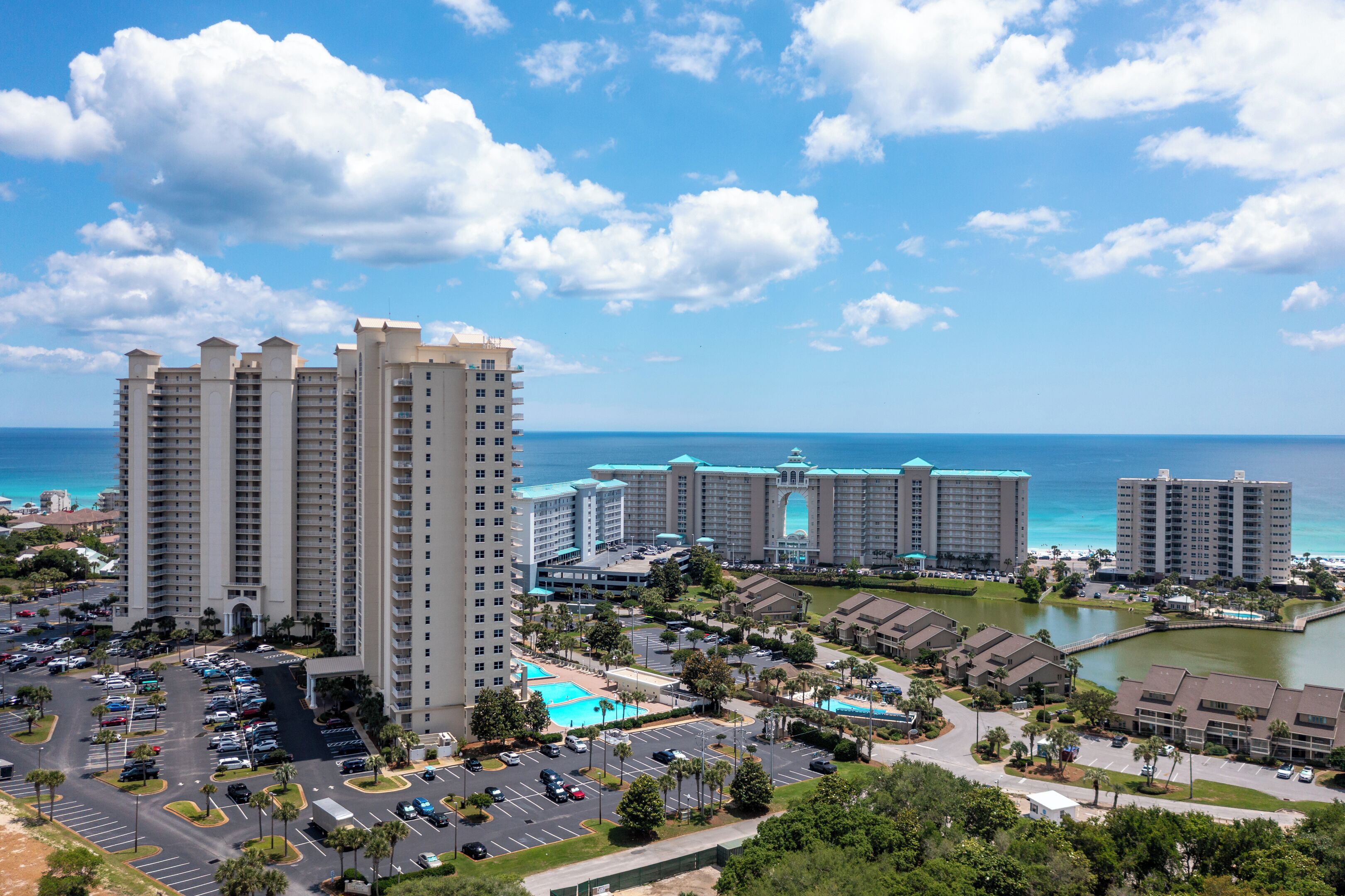 A high-rise hotel with multiple floors, a parking lot, and a view of the ocean.