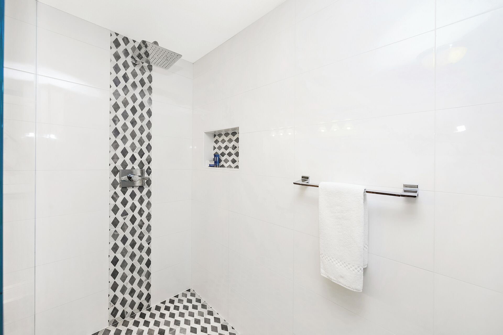 A modern bathroom with white tiles, a shower with a diamond-patterned wall, and a towel rack with a white towel.