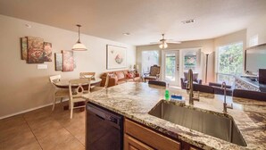 A kitchen with a dishwasher, a dining area with chairs, a sofa, and artwork on the walls.