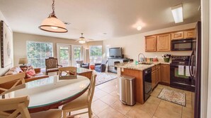 A modern kitchen with a dining area, wooden cabinets, a stainless steel refrigerator, and a TV.