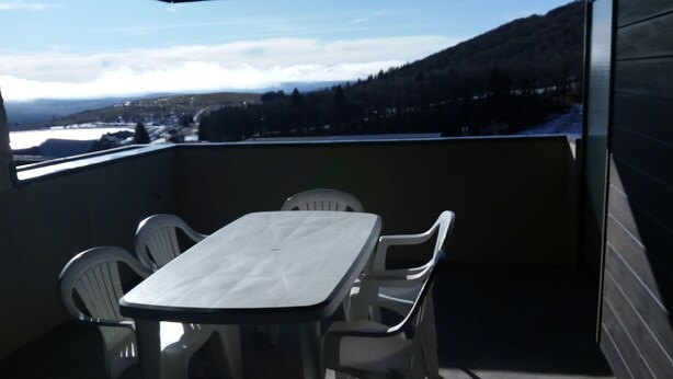 A balcony with a table and four chairs, overlooking a mountainous landscape with a view of a town below.