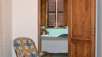 Een kamer met een schommelstoel, een houten deur, een raam met luiken en een hanglamp.