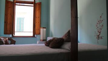 Un dormitorio con cama, ventana con contraventanas de madera, repisa montada en la pared y un adorno mural.