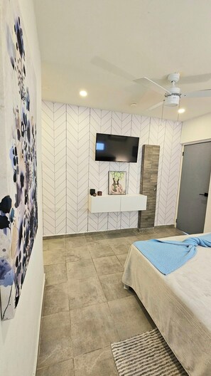 A modern bedroom with a flat-screen TV mounted on the wall, a bed with a blue blanket, and a patterned rug on the floor.