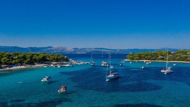 Una zona costera con barcos anclados en aguas azules cristalinas, rodeada de exuberantes árboles verdes y colinas al fondo.