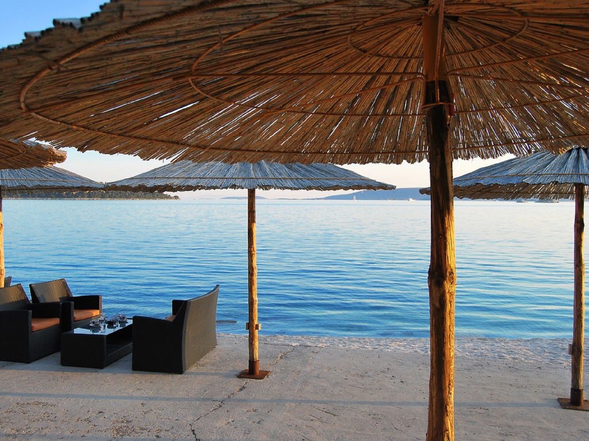 A beach with thatched umbrellas and lounge chairs.