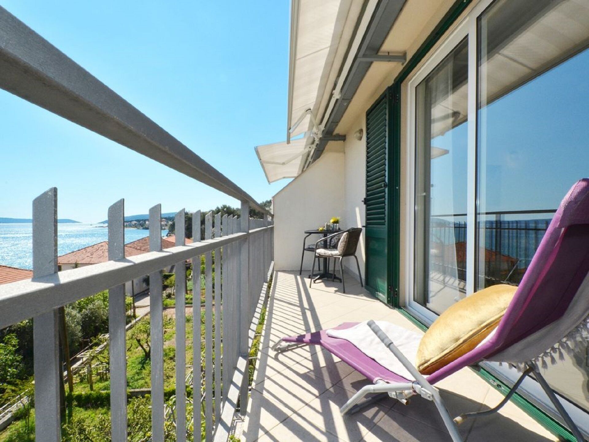 Een balkon met uitzicht op zee, een paarse stoel en een tafel met een stoel.