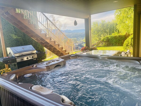 Relax in a serene hot tub with jets and a control panel, surrounded by a well-maintained garden and a beautiful view.