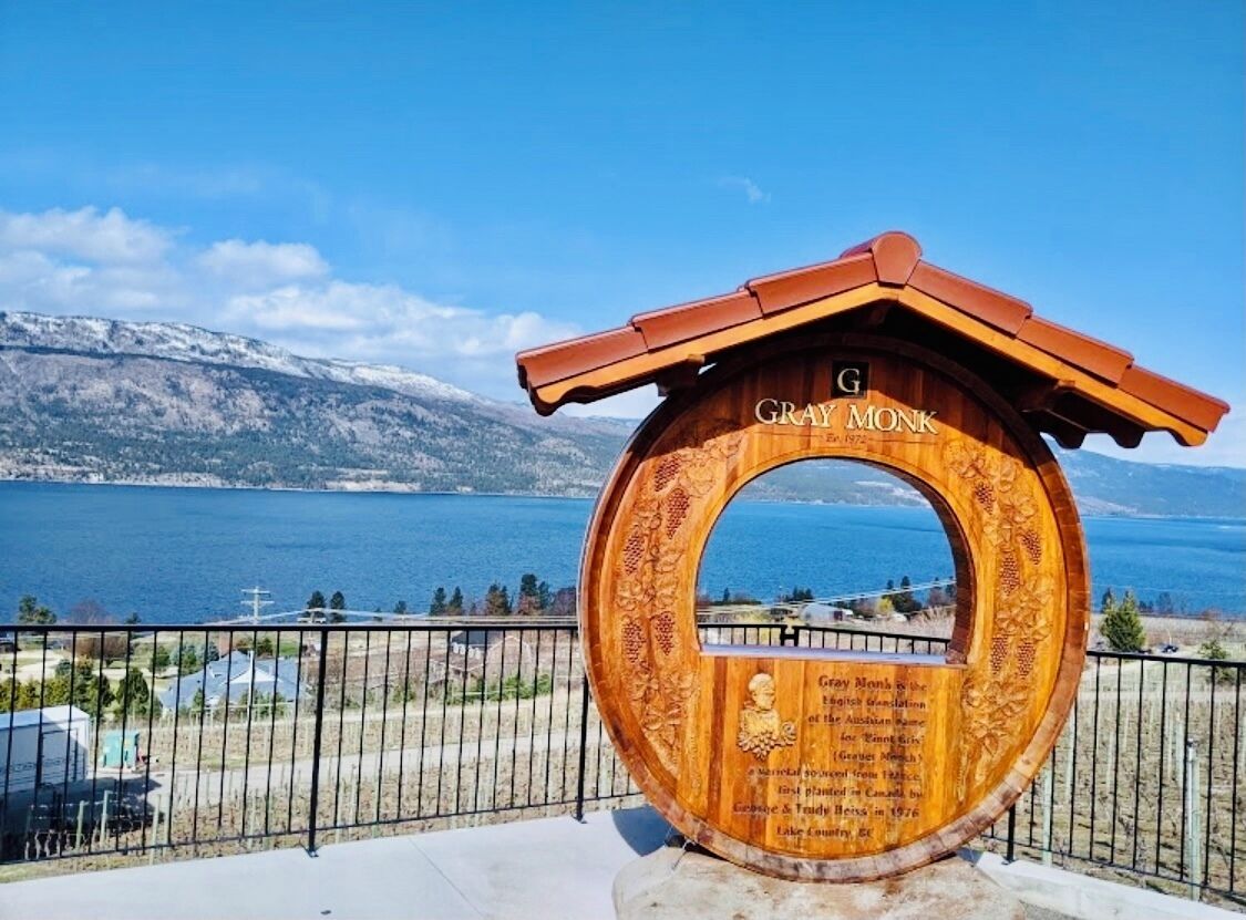 Een houten plaquette met inscripties, voor een pittoresk uitzicht op een meer en bergen.