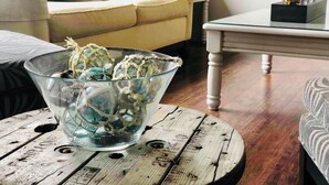 Ein Wohnzimmer mit einer Glasbowl auf einem Holztisch, einem gelben Sofa und einem weißen Tisch mit Dekoration.