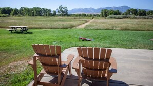 Kaksi puista Adirondack-tuolia, jotka on sijoitettu vastakkain piknikpöydän ja niityn eteen, taustalla vuoristo.