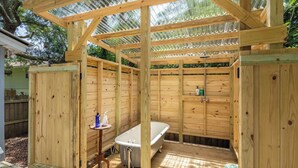 Ein Holz-Außenbad mit Badewanne, einem kleinen Tisch mit Toilettenartikeln und einer Holzterrasse.