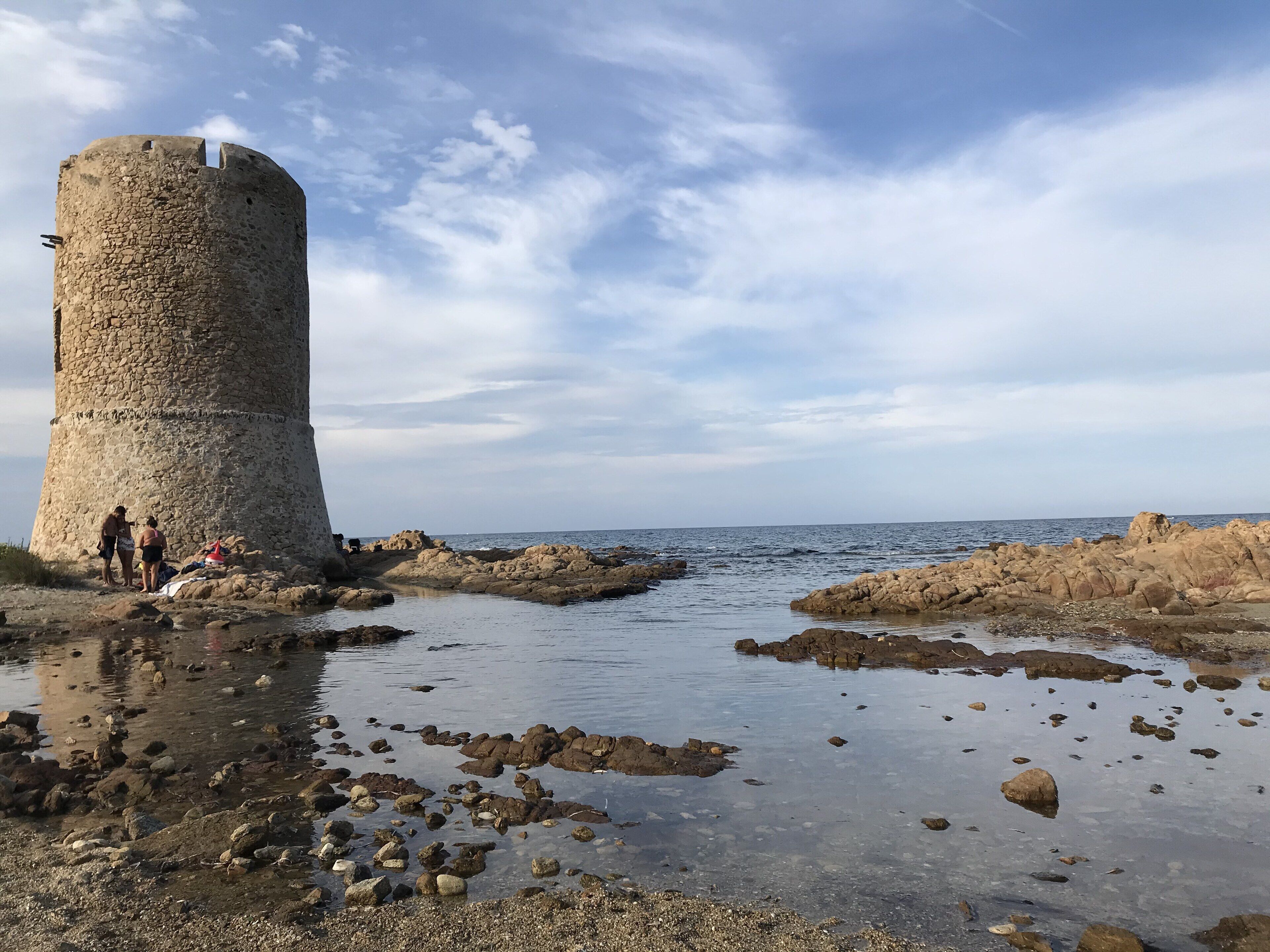 Ein Küstenturm aus Stein mit felsiger Küstenlinie und ruhiger See.