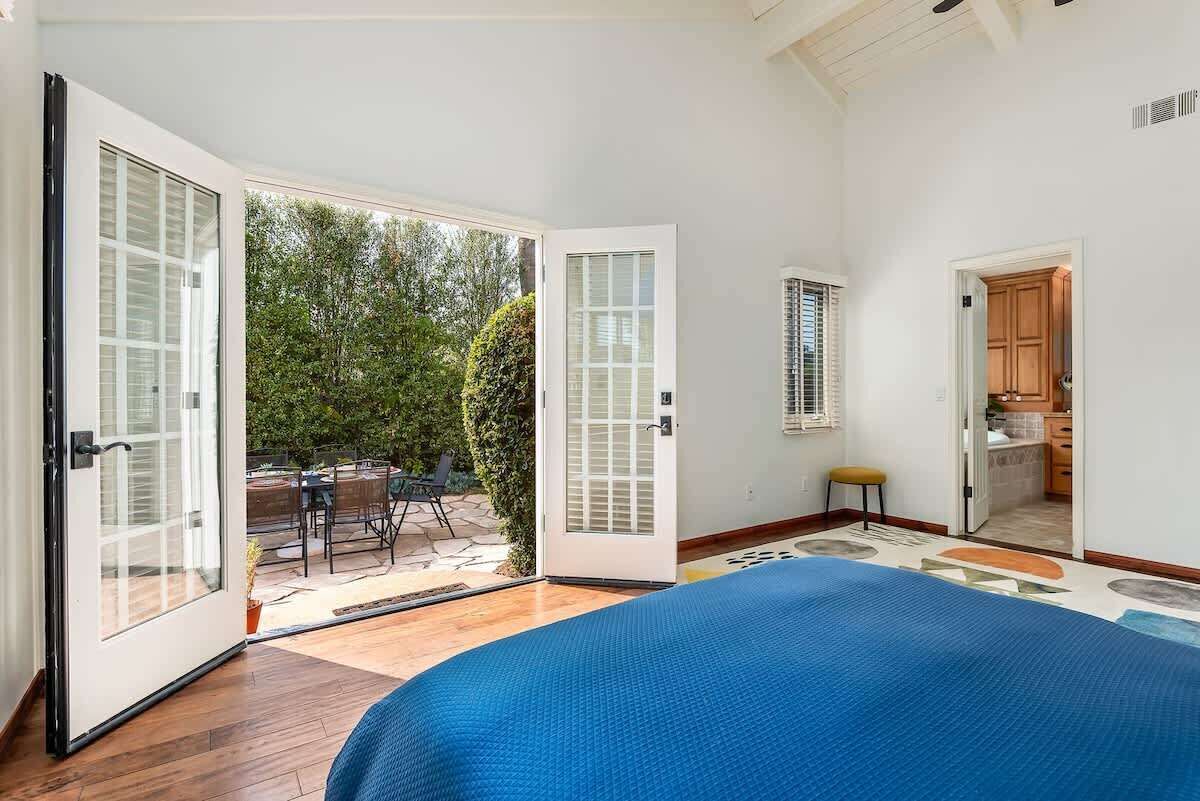 Quarto com cama grande, porta de correr de vidro para um pátio e área de cozinha visível.