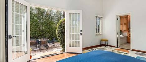 Quarto com cama grande, porta de correr de vidro para um pátio e área de cozinha visível.