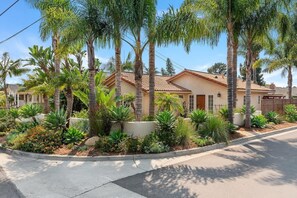 A residential house with a tiled roof, surrounded by a landscaped garden with various plants and a paved driveway.