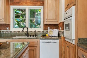 A kitchen with wooden cabinets, a white dishwasher, a white oven, and a window with a view of greenery.
