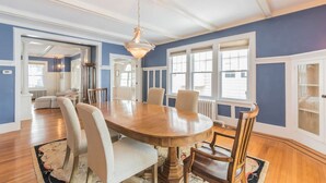 Une salle à manger avec une grande table en bois, des chaises blanches et un lustre.