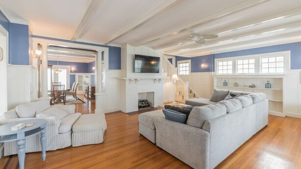 Un salon spacieux avec une cheminée, un grand canapé gris et un coin repas avec des chaises à rayures.