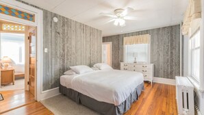 Une chambre avec un lambris en bois, un lit, une table de chevet, une commode et une fenêtre avec des rideaux.