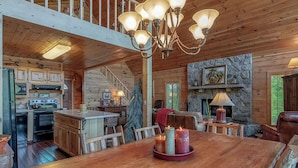 Ein Holzblockbau-Innenraum mit Küche, Essbereich und Kamin aus Stein.