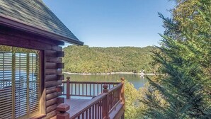 Eine Blockhütte mit einer Terrasse mit Blick auf einen See und bewaldete Hügel.