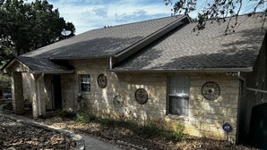 Une maison en pierre avec un toit en pente, un porche à l’avant et un petit jardin agrémenté d’un jardinière en pierre.