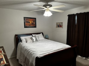 Een slaapkamer met een bed, een plafondventilator, een ingelijst kunstwerk en een raam met gordijnen.