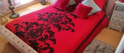 A bedroom with a tufted headboard, a red and black damask bedspread, and a fluffy rug.
