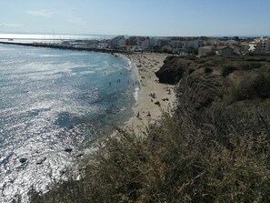 A coastal beach with a rocky shoreline, a marina in the background, and buildings along the coast.