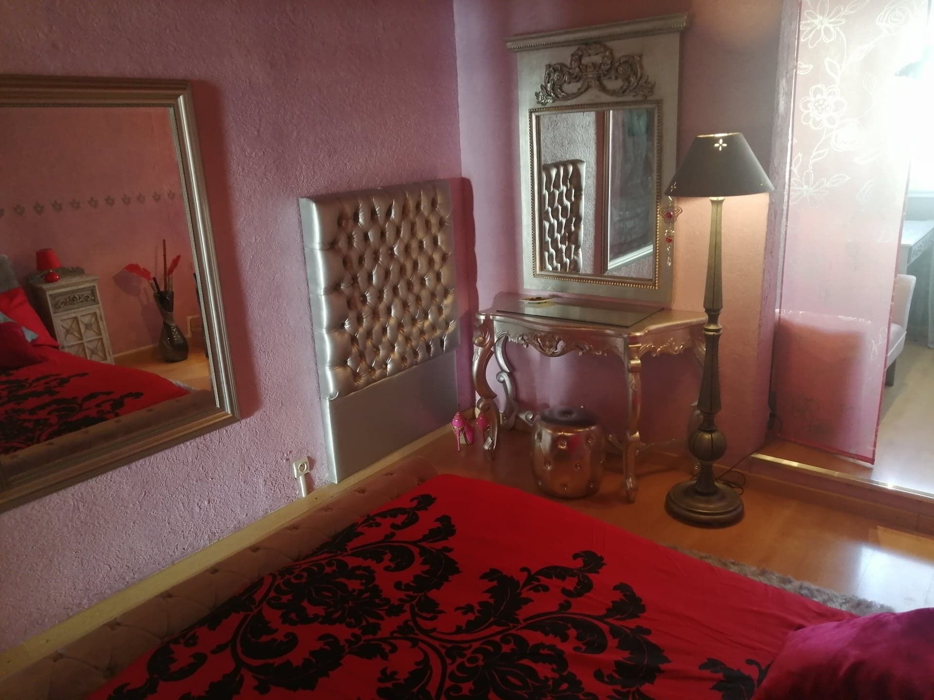 A bedroom with a tufted headboard, a bedside table with a lamp, and a mirror.