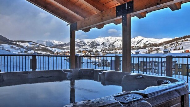 Un área de hidromasaje con una pérgola de madera, vistas a montañas nevadas y una masa de agua al fondo.